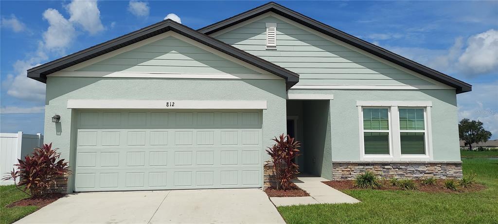 A single-story house with a light green exterior, a two-car garage, and stone facade accents — 812 KINGS PINE COURT, RUSKIN, FL