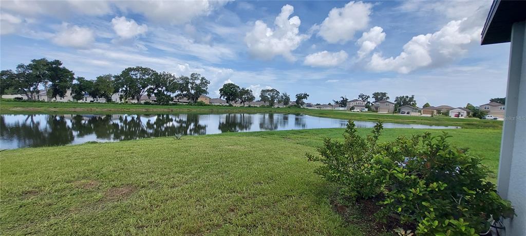 A grassy backyard overlooks a pond with houses visible in the distance under a cloudy sky — 812 KINGS PINE COURT, RUSKIN, FL