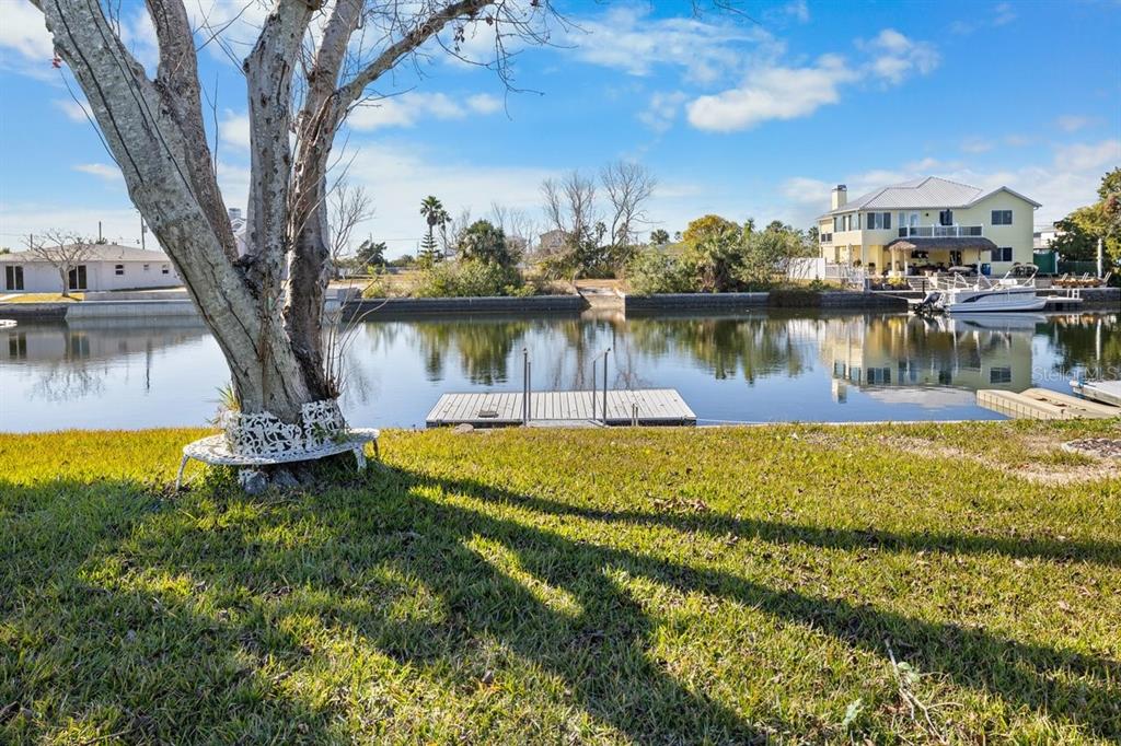 A grassy backyard features a tree with a bench overlooking a canal and boat dock — 4117 TAMPICO TRAIL, HERNANDO BEACH, FL