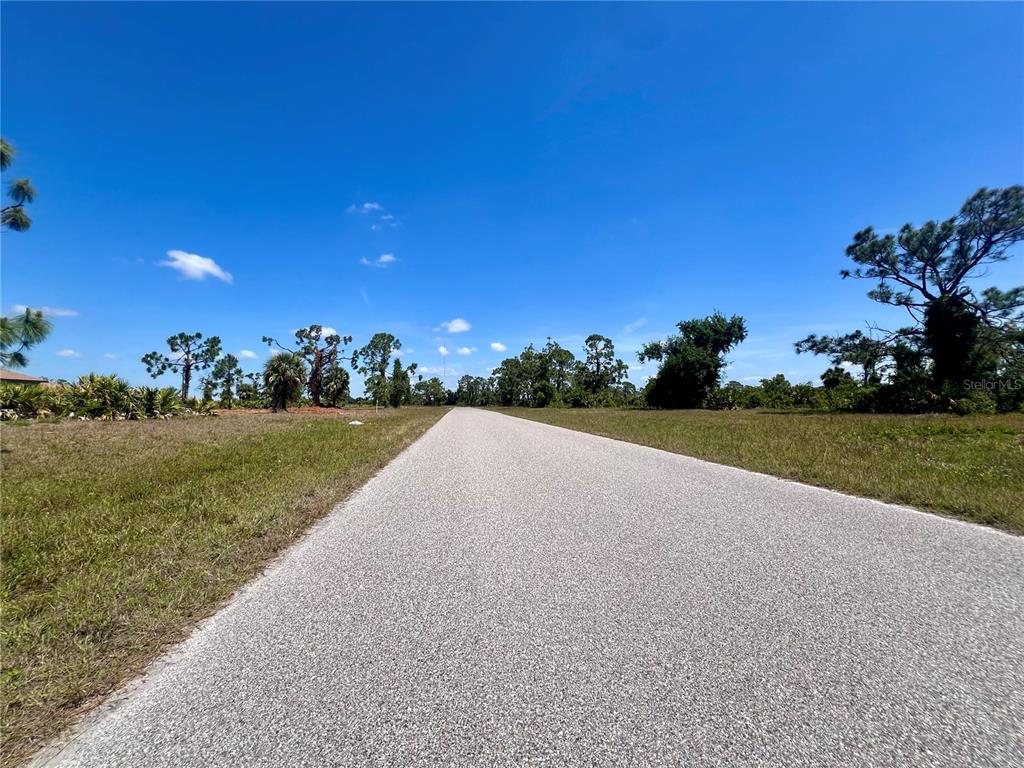 A paved road stretches through a grassy, undeveloped lot under a clear blue sky — 36 COXSWAIN DRIVE, PLACIDA, FL
