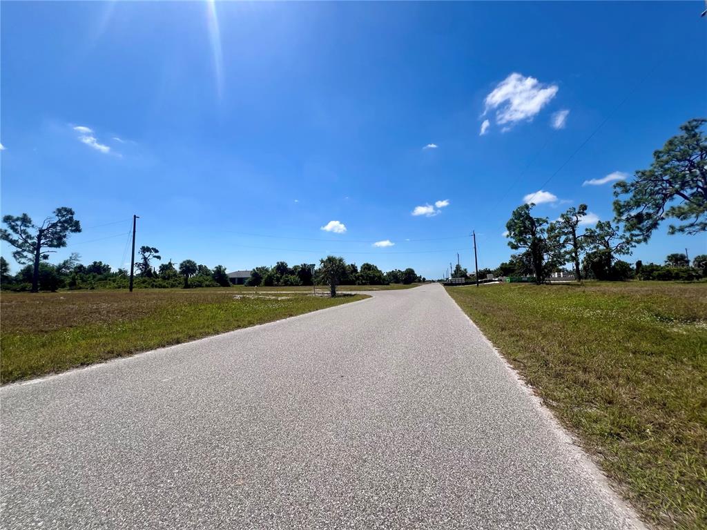 A paved road stretches through a grassy, undeveloped lot under a bright blue sky — 36 COXSWAIN DRIVE, PLACIDA, FL