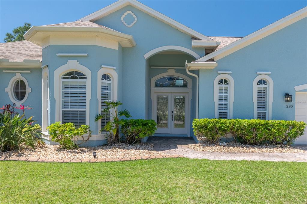 A light blue house exterior features a double front door, arched windows, and landscaping — 230 RIDGEMONT CIRCLE, PALM BAY, FL