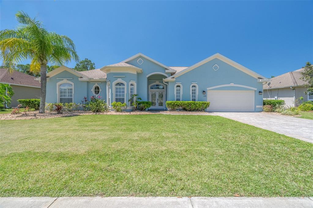 A light blue single-story house features a palm tree, arched windows, and a two-car garage — 230 RIDGEMONT CIRCLE, PALM BAY, FL