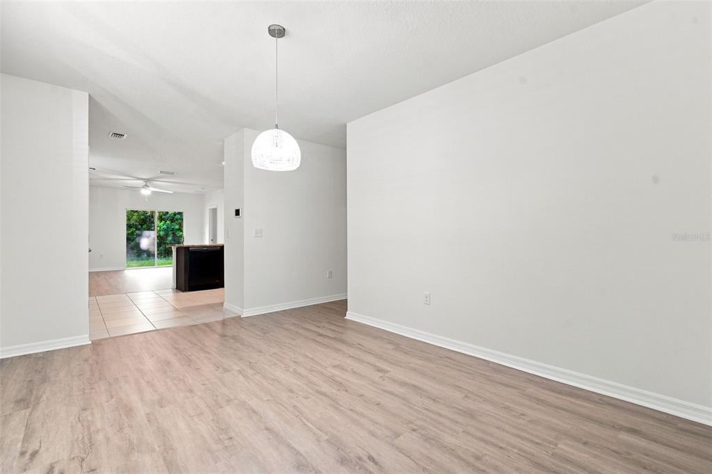 A dining area with light wood-look flooring leads to a kitchen with tile flooring — 10920 CARLTON FIELDS DRIVE, RIVERVIEW, FL