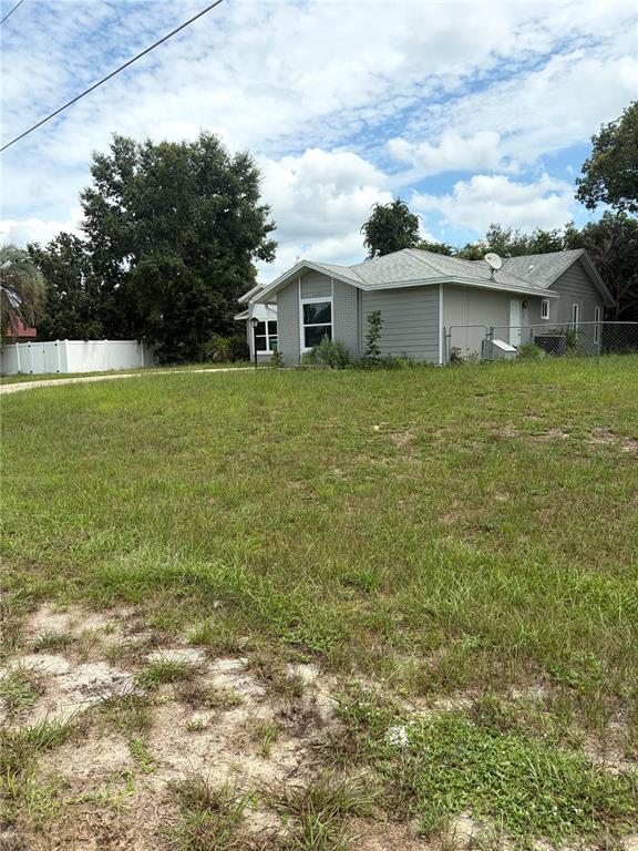 A gray, single-story house with a shingled roof sits on a large, grassy lot — 1499 COURTLAND BOULEVARD, DELTONA, FL