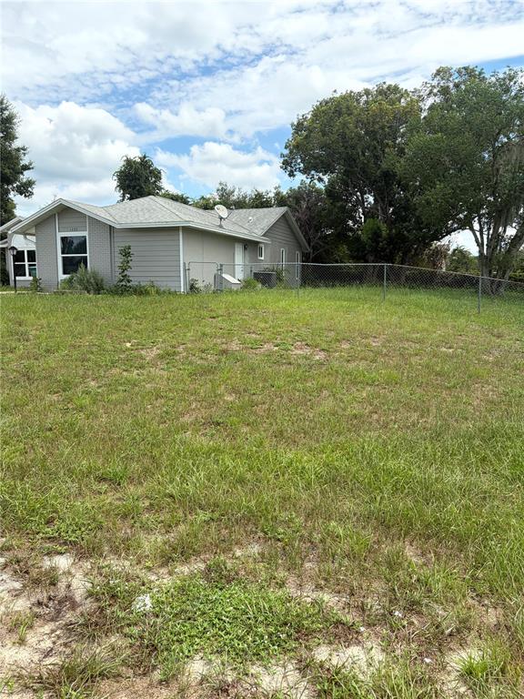 A single-story house with light-colored siding stands behind a chain-link fence and grassy yard — 1499 COURTLAND BOULEVARD, DELTONA, FL