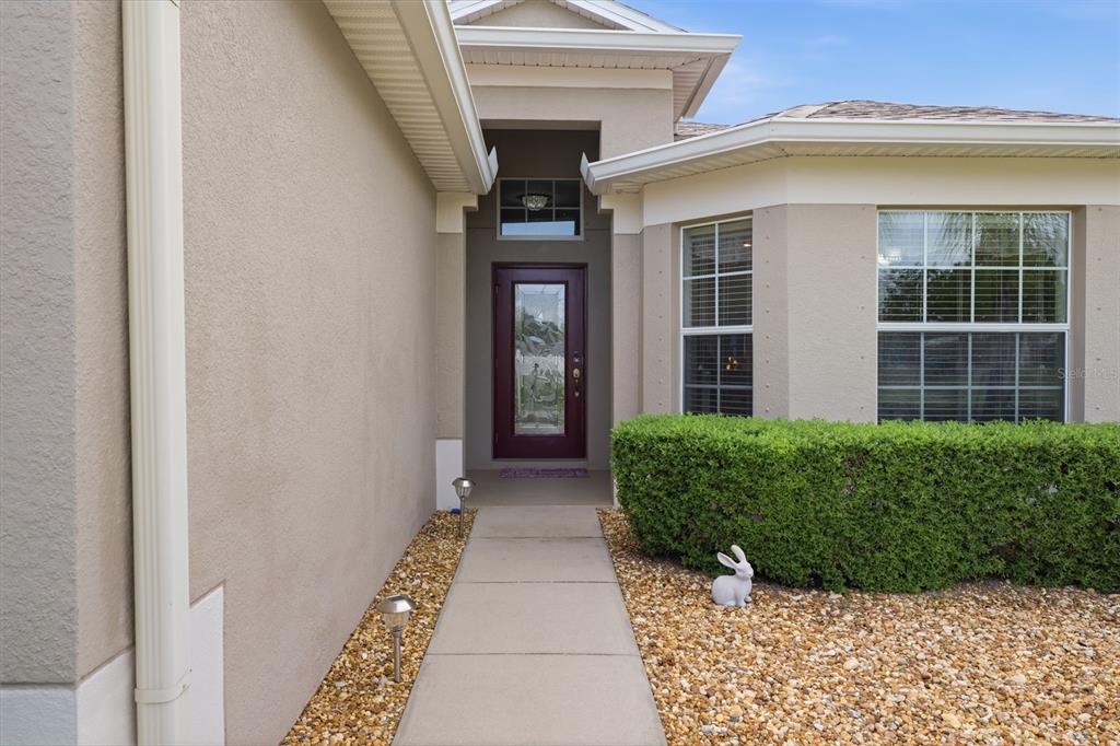A concrete walkway leads to the front entrance of a house with beige stucco walls — 10114 IVES LOOP, HUDSON, FL