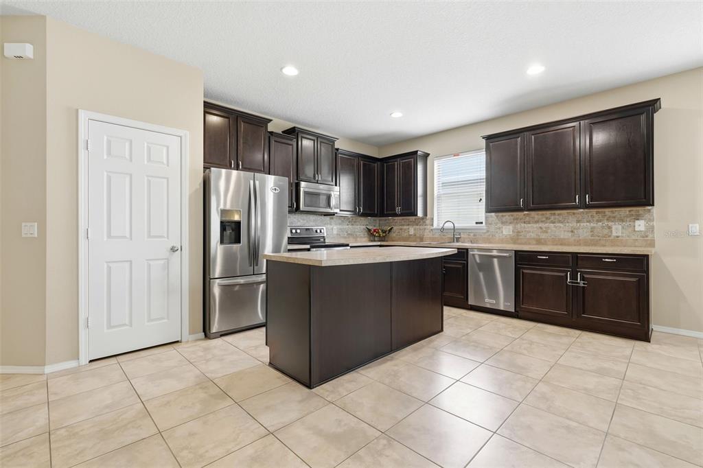 A kitchen features dark wood cabinets, stainless steel appliances, a center island, and tile flooring — 20945 OLDENBURG LOOP, MOUNT DORA, FL