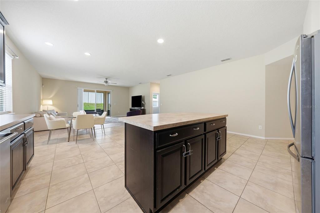 A kitchen island with dark cabinets and a light countertop sits in an open-concept room — 20945 OLDENBURG LOOP, MOUNT DORA, FL