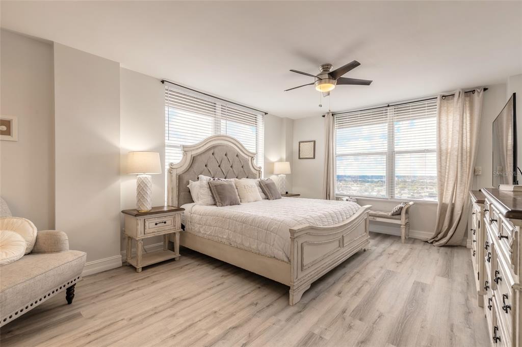 A bedroom features a tufted headboard bed, light wood flooring, and large windows with blinds — 1575 OCEAN SHORE BOULEVARD UNIT J070, ORMOND BEACH, FL