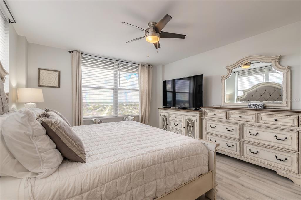 A bedroom features a white bed, a dresser with a mirror, and a ceiling fan — 1575 OCEAN SHORE BOULEVARD UNIT J070, ORMOND BEACH, FL