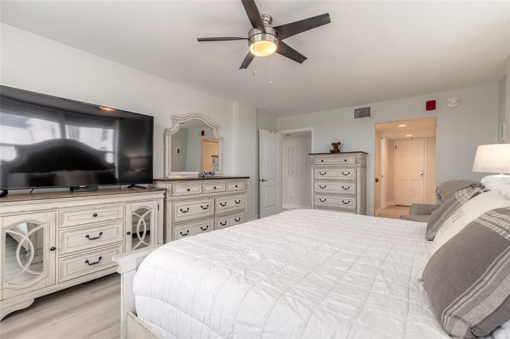 A bedroom features a white bed, matching dressers, a large television, and a ceiling fan — 1575 OCEAN SHORE BOULEVARD UNIT J070, ORMOND BEACH, FL