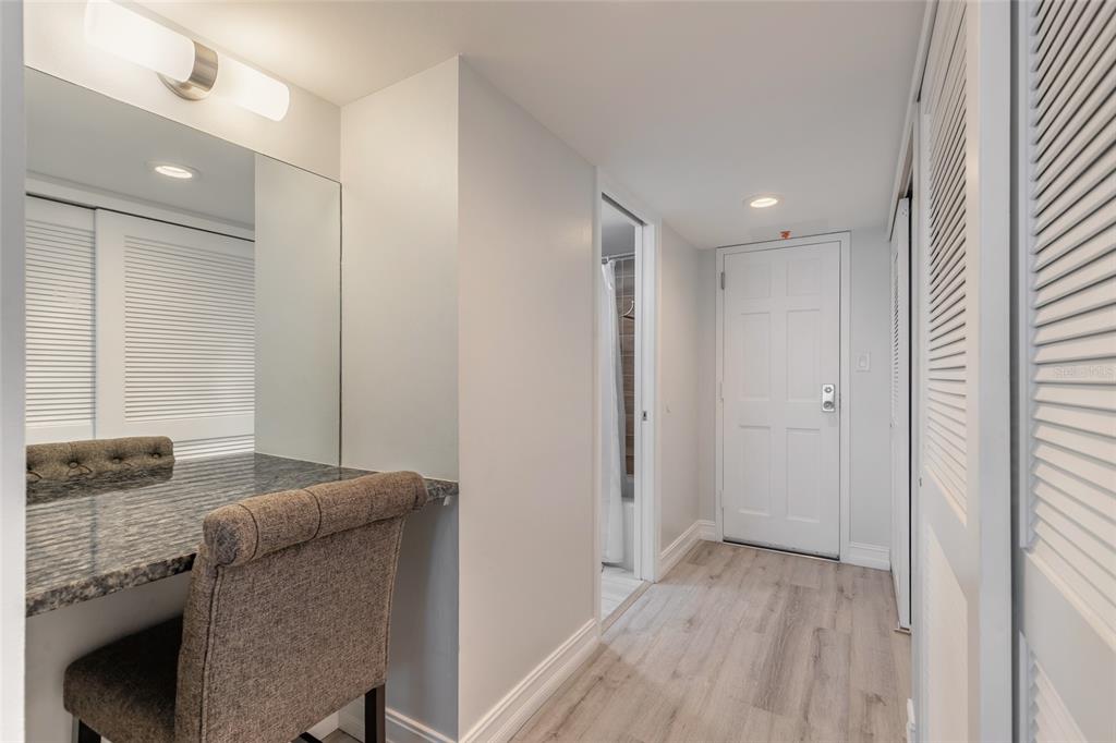 A vanity area with a mirror and chair sits beside a hallway leading to a bathroom — 1575 OCEAN SHORE BOULEVARD UNIT J070, ORMOND BEACH, FL