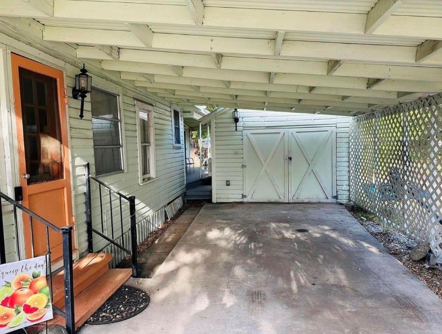 A covered carport leads to a house entrance with an orange door and wooden steps — 1121 ORANGE AVENUE, DUNEDIN, FL