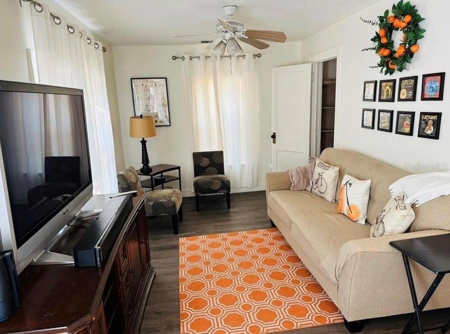 A living room features a beige sofa, orange geometric rug, television, and a ceiling fan — 1121 ORANGE AVENUE, DUNEDIN, FL