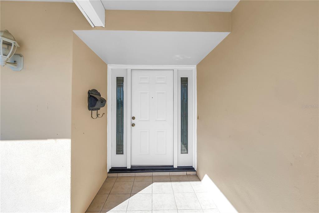 A white front door with sidelights is centered on a tiled porch with beige walls — 2053 DOLPHIN BOULEVARD S, ST PETERSBURG, FL