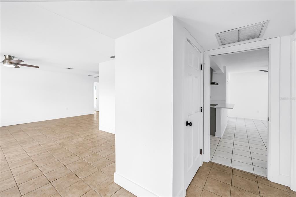 A bright room with tan tile flooring leads into a kitchen through a white doorway — 2053 DOLPHIN BOULEVARD S, ST PETERSBURG, FL