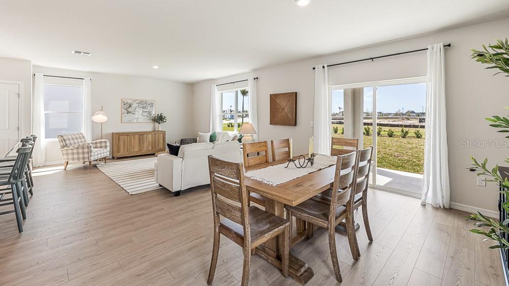 An open-concept living and dining area features light wood flooring, neutral walls, and sliding doors — 1733 COBB TRAIL, PARRISH, FL