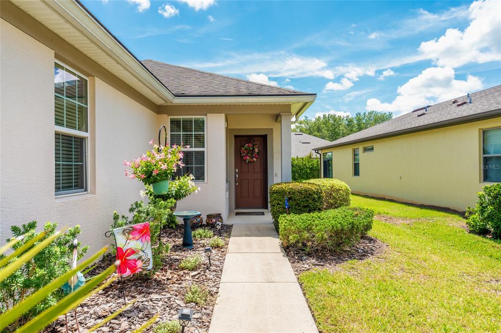 A concrete walkway leads to the front entrance of a beige house with a brown door — 9098 SW 70TH LOOP, OCALA, FL