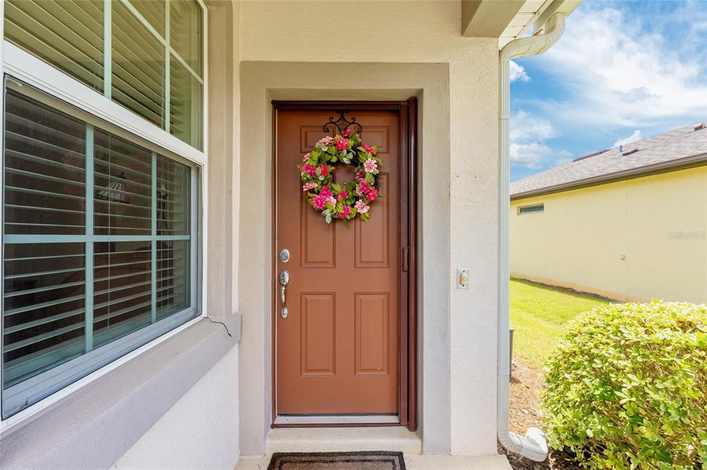 A brown front door with a floral wreath sits beside a window on a porch — 9098 SW 70TH LOOP, OCALA, FL