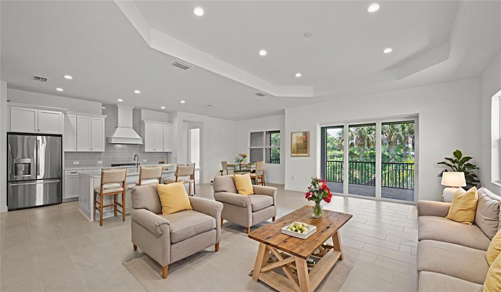 An open-concept living room and kitchen featuring light tile floors and sliding glass balcony doors — 11540 VERANDAH PALM COURT, FORT MYERS, FL