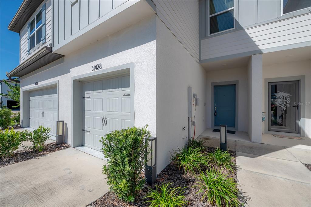 An exterior view of a two-story townhouse with a garage and a blue front door — 31428 AMBERVIEW BEND, WESLEY CHAPEL, FL