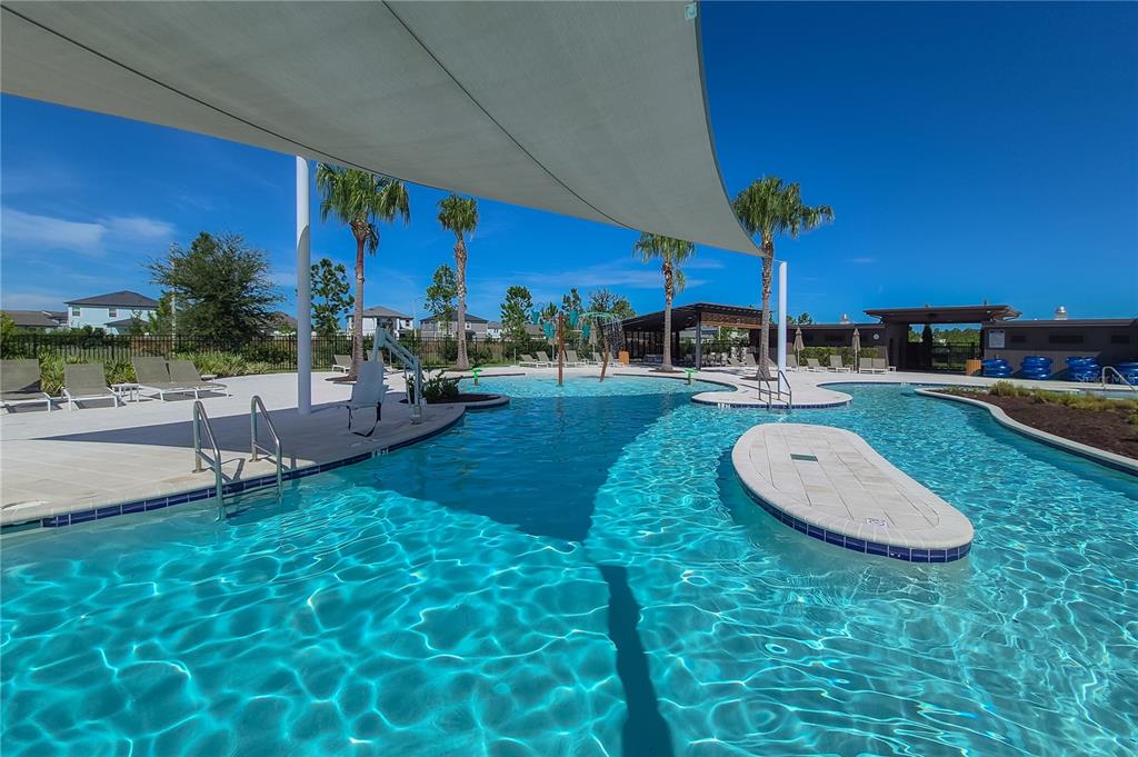 An outdoor swimming pool with a shade sail, lounge chairs, and palm trees — 31428 AMBERVIEW BEND, WESLEY CHAPEL, FL