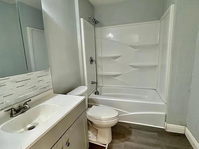 A bathroom features a white vanity, a toilet, and a tub-shower combination with built-in shelving — 1605 36TH STREET NW, WINTER HAVEN, FL