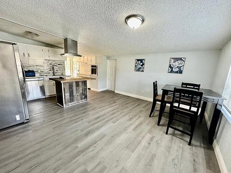 A kitchen and dining area feature gray wood-look flooring, white cabinets, and a kitchen island — 1605 36TH STREET NW, WINTER HAVEN, FL