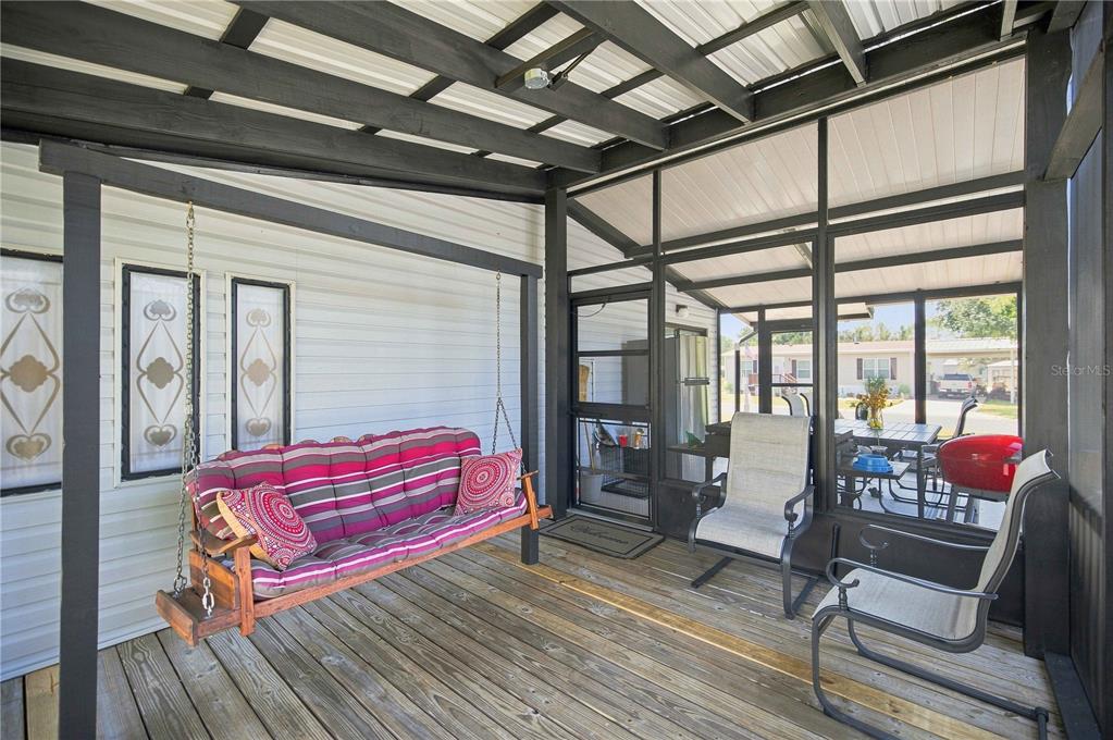 A screened-in porch features a wooden deck, a hanging swing, and outdoor chairs — 8385 N SHADY FORK WAY, DUNNELLON, FL