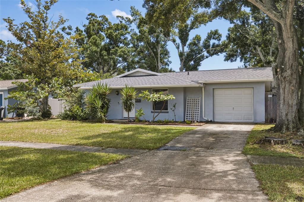 A single-story gray house with a one-car garage and a concrete driveway under large trees — 2940 47TH AVENUE S, ST PETERSBURG, FL