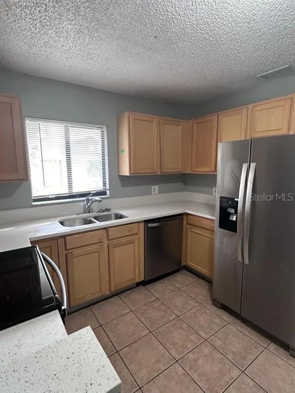 A kitchen features light wood cabinets, stainless steel appliances, white countertops, and tiled flooring — 90 HIDDEN LAKE DRIVE UNIT 124, SANFORD, FL