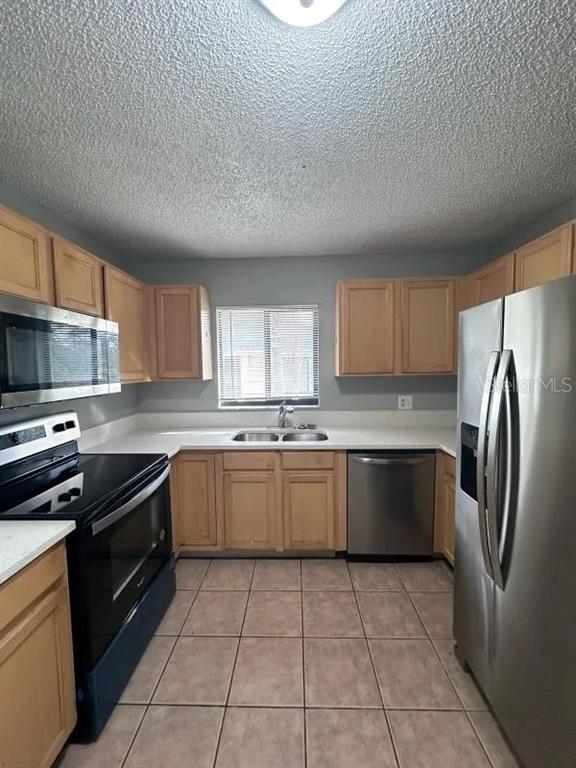 A kitchen features light wood cabinets, stainless steel appliances, a double sink, and tile flooring — 90 HIDDEN LAKE DRIVE UNIT 124, SANFORD, FL