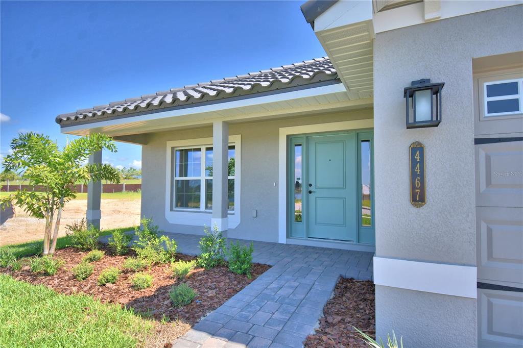 A light gray house exterior features a teal front door and a paver walkway — 4467 JULIANA LAKE DRIVE, AUBURNDALE, FL