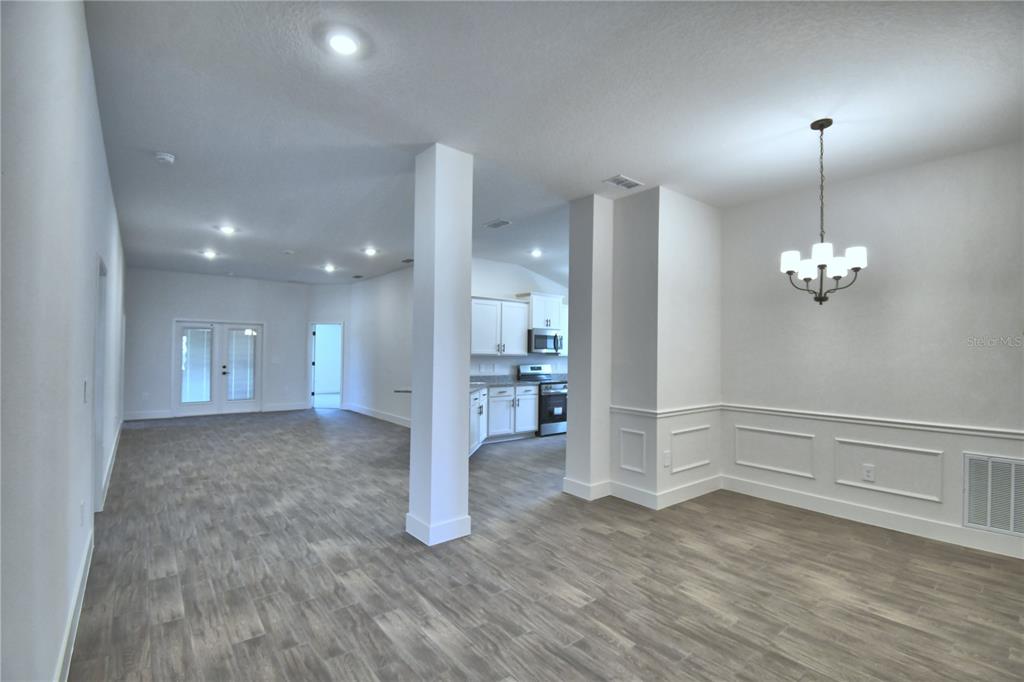 An open-concept living and dining area features white walls, wainscoting, and gray wood-look flooring — 4467 JULIANA LAKE DRIVE, AUBURNDALE, FL