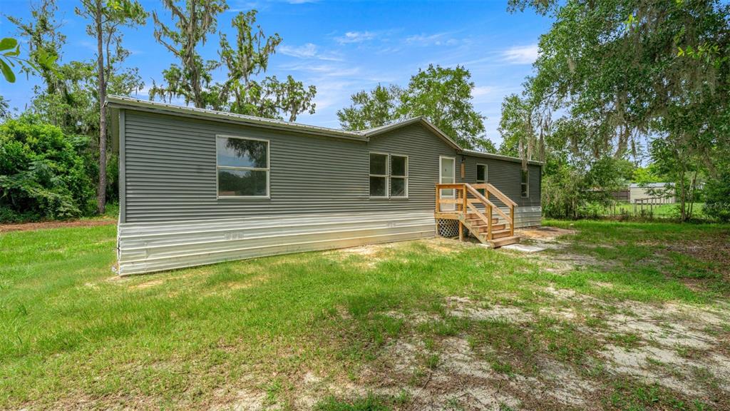 A gray manufactured home with a wooden staircase sits on a grassy lot with trees — 5363 ORANGE STREET, HAMPTON, FL