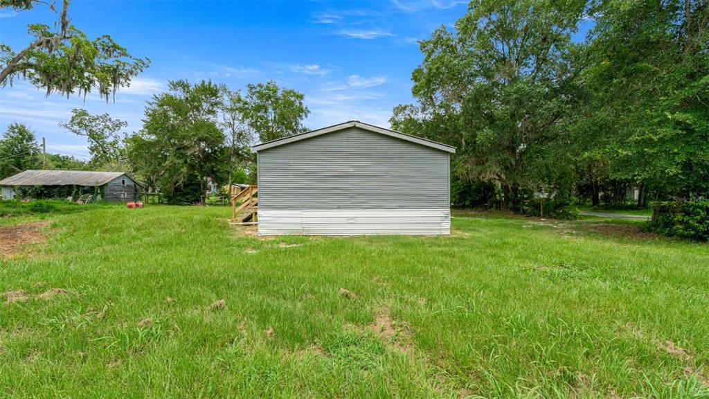 A gray mobile home sits in a grassy yard with trees in the background — 5363 ORANGE STREET, HAMPTON, FL