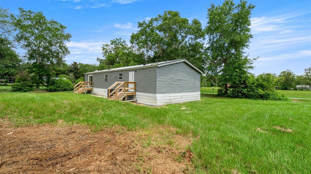 A gray manufactured home with wooden stairs sits on a large, grassy lot — 5363 ORANGE STREET, HAMPTON, FL