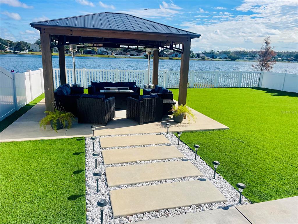A backyard gazebo with outdoor furniture sits on a patio overlooking a lake — 2830 MUSKY MINT DRIVE, LAND O LAKES, FL