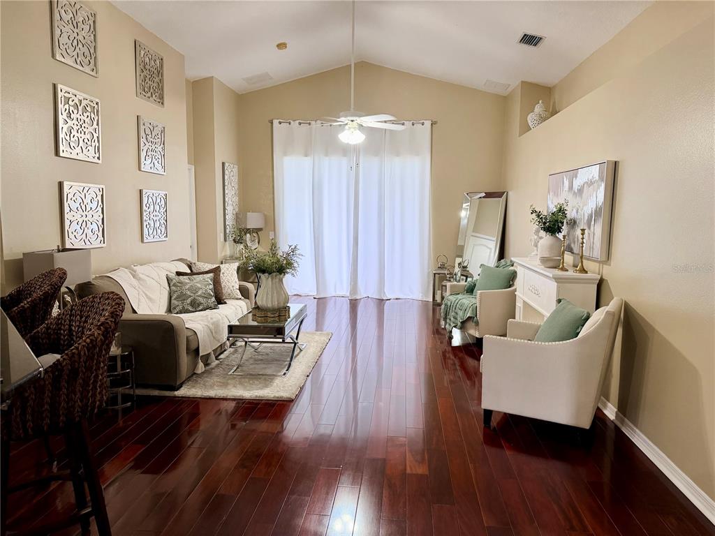 A living room features dark hardwood floors, vaulted ceilings, and a sofa facing two armchairs — 2830 MUSKY MINT DRIVE, LAND O LAKES, FL