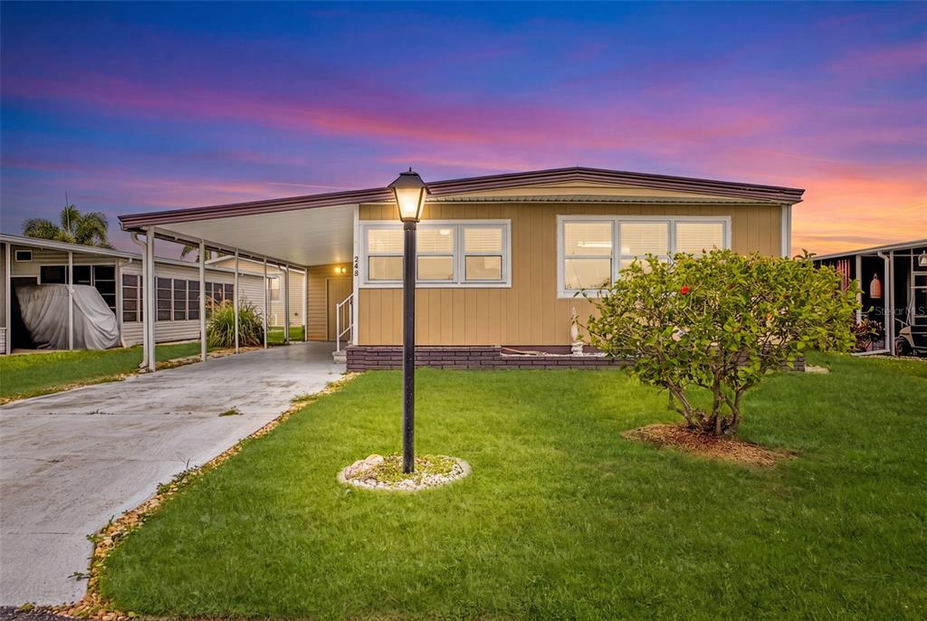 A single-story manufactured home with a tan exterior, a carport, and a front lawn — 248 LA ROSAS, NORTH PORT, FL