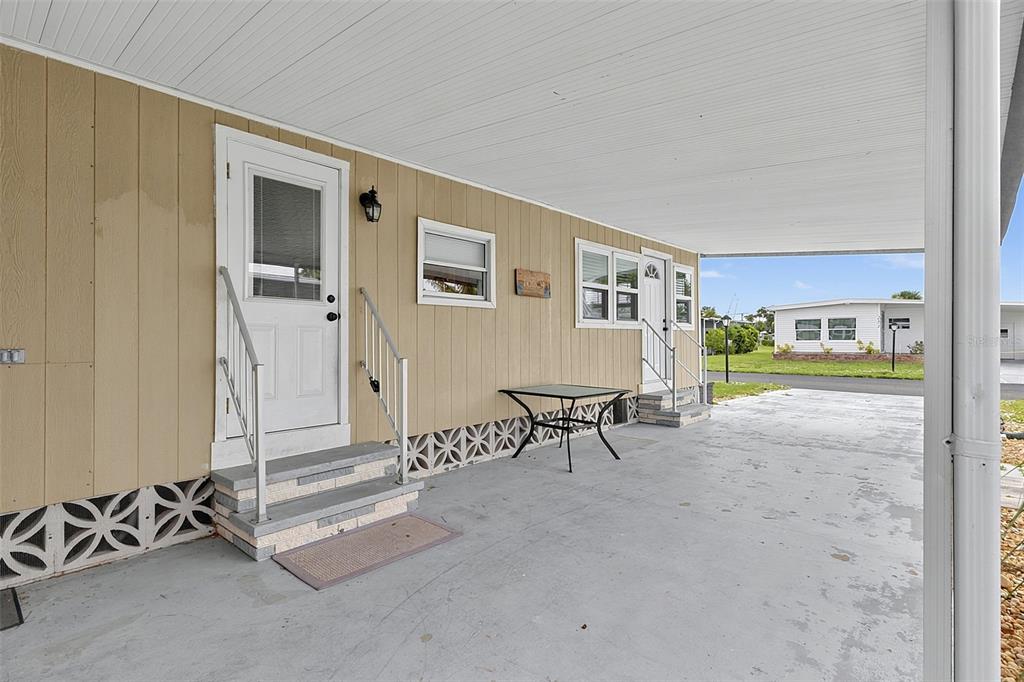A tan mobile home exterior features a covered concrete carport, two entry doors, and stairs — 248 LA ROSAS, NORTH PORT, FL