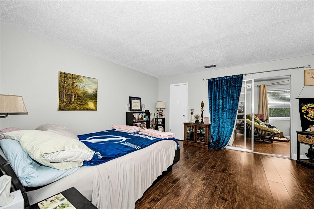A bedroom with wood-look flooring, a bed with a blue blanket, and a sliding glass door — 5060 76TH AVENUE N UNIT 401, PINELLAS PARK, FL