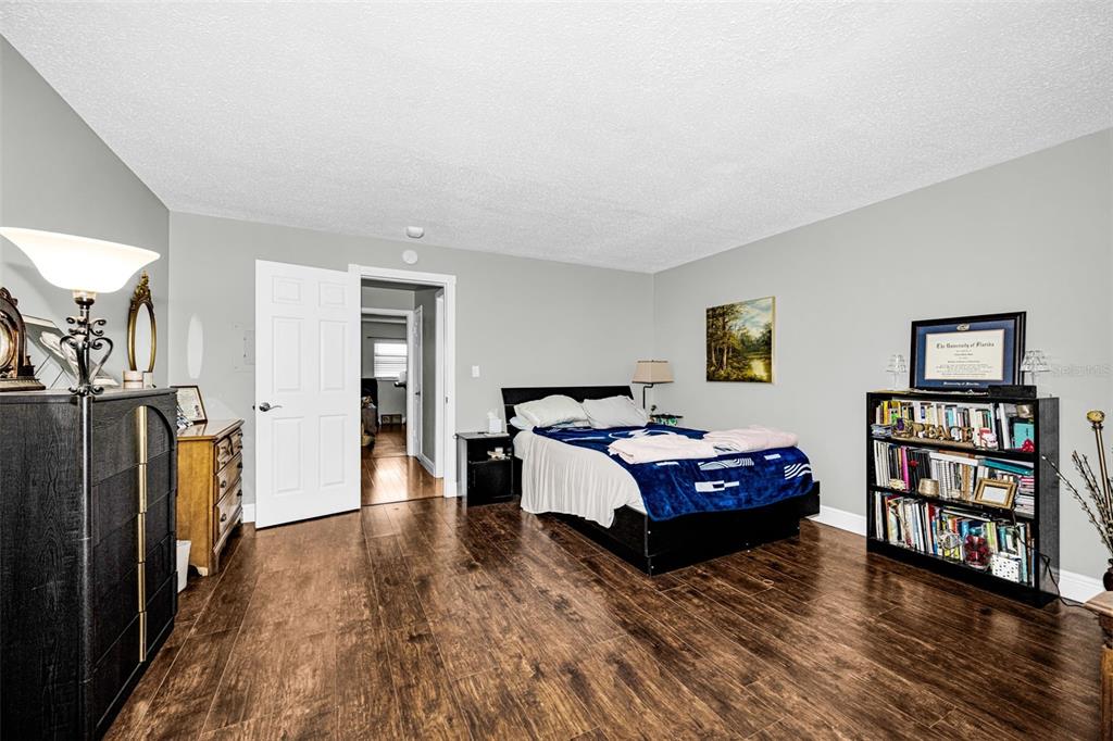 A bedroom features wood-look flooring, a bed, a bookshelf, and a dresser under a lamp — 5060 76TH AVENUE N UNIT 401, PINELLAS PARK, FL