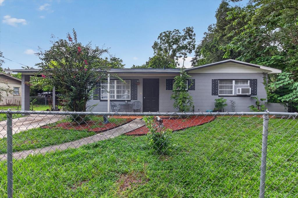 A single-story gray house with a front porch, carport, and chain-link fence in the yard — 21385 LEHOUIER DRIVE, BROOKSVILLE, FL