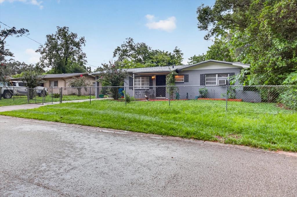 A gray, single-story house with a chain-link fence sits behind a grassy front yard — 21385 LEHOUIER DRIVE, BROOKSVILLE, FL