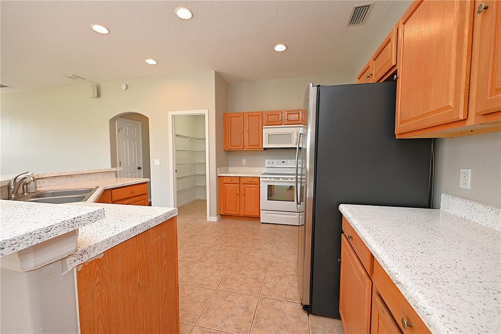 A kitchen features light wood cabinets, white speckled countertops, tile flooring, and stainless steel appliances — 125 COSTA LOOP, AUBURNDALE, FL