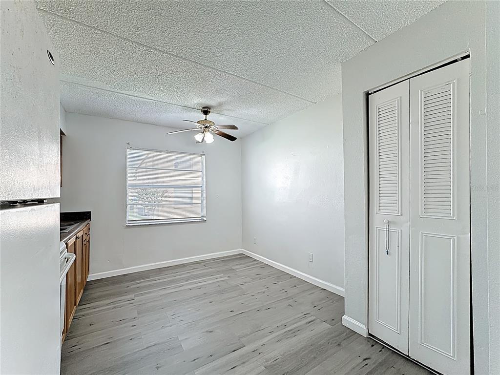 A kitchen and dining area with gray wood-look flooring, white walls, and a ceiling fan — 694 MICHIGAN COURT UNIT 4, ST CLOUD, FL