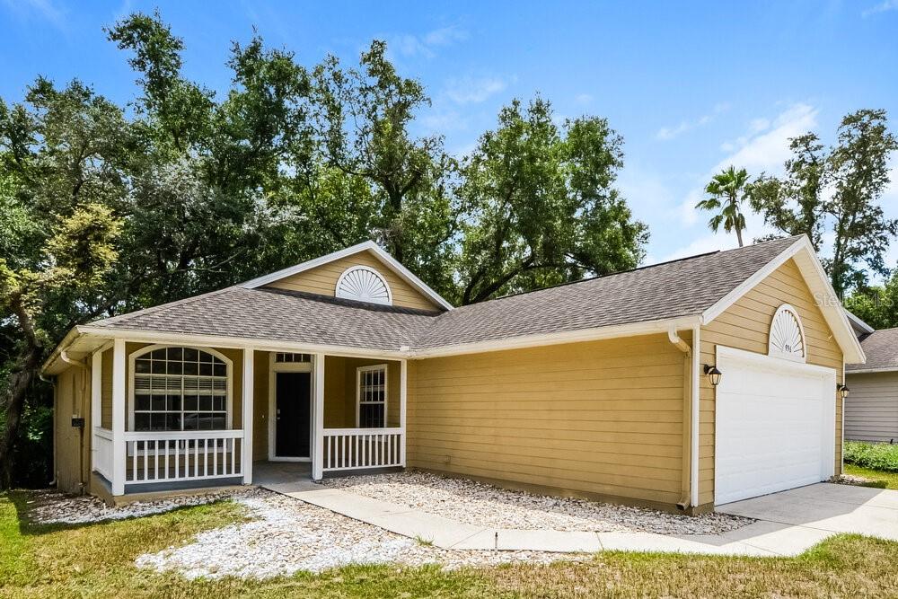 A tan, single-story house with a white garage door, front porch, and gravel landscaping — 996 MAPLE COURT, APOPKA, FL