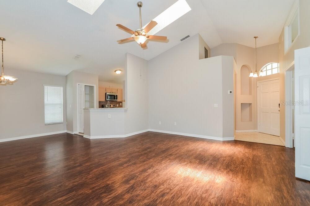 A spacious living room with vaulted ceilings, a ceiling fan, and dark wood-look flooring — 996 MAPLE COURT, APOPKA, FL